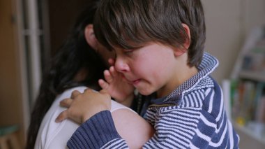 Genç çocuk üzgün ve ağlıyor, onlar sarılırken annesi tarafından teselli ediliyor. Çocuk üzgün ve duygusal, destekleyici ebeveynden huzur ve bakım istiyor.