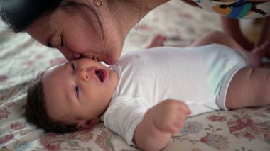 Anne-baba sevgi dolu bir şekilde yatakta uzanmış bebeği öpüyor, şefkat ve sıcaklık gösteriyor, bebeğin geniş gözleri, şefkat ve yakınlık dolu bir ev ortamında baktığı anlar