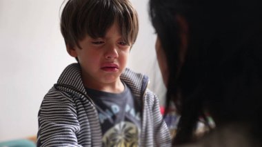 Genç bir çocuk ağlıyor, annesine bakarken görünür bir şekilde üzgün ve sıkıntılı. Bir anne ve çocuk arasındaki duygusal hassasiyet ve üzüntü anı.