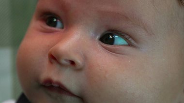 Bebek yüzüne aşırı yakın çekim, gözlere ve yumuşak yüz hatlarına odaklanma. Meraklı bir bebeğin kapalı alanda yukarı doğru bakışının detaylı görüntüsü.