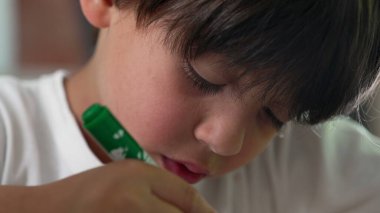 Close-up of young boy concentrating as he colors with a green marker, fully focused on his artwork, showcasing creativity and careful attention clipart