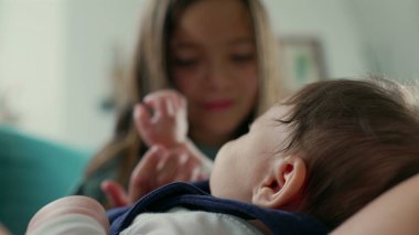 Kucağında büyük bir çocuğun nazikçe uzanıp bebeğe dokunduğu ve kardeşler arasındaki hassas bağı yakaladığı bir bebeğin yakın çekimi.