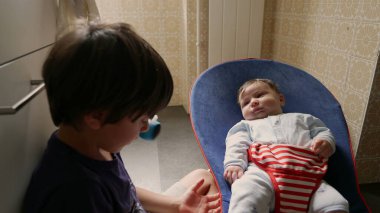 Büyük kardeş, bebek kardeşiyle yatakta yatar, onlara nazikçe sarılır ve bağlanır, şefkatli ve samimi bir aile anı yaratır.