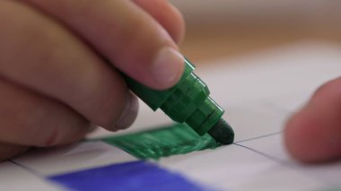 Bir şebeke içinde renk vermek için yeşil işaret kullanan bir çocuğun elinin yakın plan görüntüsü, çizimin ayrıntılı hareketi ve hassasiyetine odaklanıyor