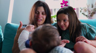 Anne ve kızı gülüyor ve eğleniyorlar. Bir bebek anne kucağında dinleniyor. Bir aile olarak birbirlerine bağlanıyorlar.