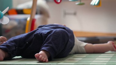 Bir bebeğin oyun hasırının üzerine uzanmış, rahat bir ev ortamında oyun saatinde bebeğin bacaklarını ve ayaklarını rahat bir pozisyonda gösteriyor.