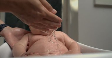 Banyo sırasında bebeğin karnından yavaşça akan su, bebek sakin ve rahatlamış, banyo bakımına odaklanmış. 800 fps yavaş çekim