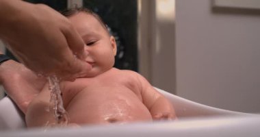 Banyo sırasında bebek bedeninden akan su, bebek sakin ve aşağıya bakan huzur verici ve rahatlatıcı banyo bakımı. 800 fps yavaş çekim