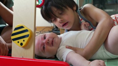 Genç bir çocuk yerde bir bebeğin yanında yatıyor, evde oyun sırasında bebekle nazikçe iletişim kurarken şefkat ve bağlılık gösteriyor.