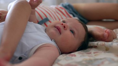 Bebeğin yatağın üzerine uzanmış, daha büyük bir çocuğun eli bebeğin kafasında yavaşça dinleniyor. Kardeş bağını ve iç mekanda barışçıl bir etkileşimi yakalamak