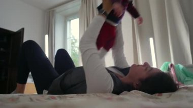 Anne yatakta yatarken bebeği kaldırıyor, oyun oynuyor ve aile evinde kaynaşıyor, birlikte eğleniyor, sevgi ve sevgi dolu bir bağ kuruyor.