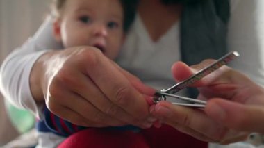 Anne bebeğin tırnaklarını nazikçe tırnak makasıyla kesiyor, ebeveynlik anlarını yakından çekiyor, bebek sakince izliyor, hijyen ve bakım yapıyor.