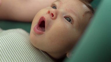 Meraklı ve sakin bir ifadeyle yukarı bakan bir bebeğin yakın çekimi. Bebeğin geniş gözleri, huzurlu ve samimi bir ortamda merak ve masumiyet hissini yansıtır.