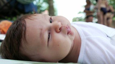 Bebek dışarıdaki bir battaniyeye uzanıyor. Etrafa bakarken yavaşça gülümsüyor. Doğal park ortamı, sakin ve açık bir ortamda çocukluk zamanlarının neşesini ve mucizesini yakalar.