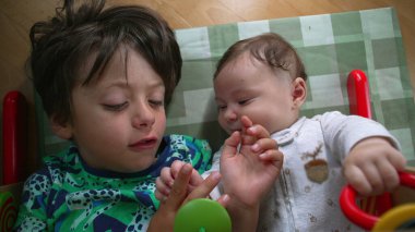 Genç bir çocuk ve bebek yerde yatıyor, birbirlerine bakıyorlar, sevinçle gülümseyen bebek, neşeli ve neşeli bir kardeşlik bağı kurma anını vurguluyorlar.