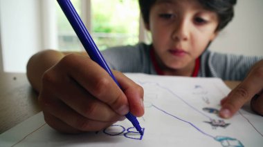 Bir çalışma kağıdındaki kelimelerin izini sürmeye odaklanan genç çocuk, erken okuma yazma becerileri ve hassas motor koordinasyonunu geliştiriyor, ev ortamında görevi tamamlamaya derinden konsantre oluyor.