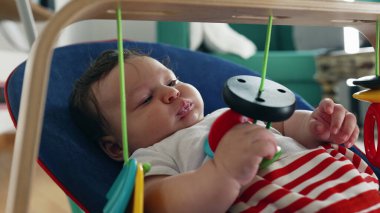 Bebek bir fedainin içinde uzanıyor, oyuncaklara uzanıyor ve dokunuyor, merakla duyusal nesneleri keşfediyor, sakin ve rahat bir ortamda odaklanmayı ve bağlanmayı ifade ediyor.