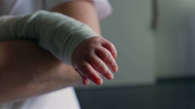 Bebeğin eli yavaşça uzanıyor, parmakları hafifçe kıvrılıyor, annesinin kollarında yatarken hassas ve samimi bir keşif ve hareket anında.