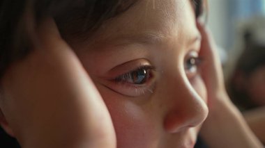 Genç oğlanın gözünün yakın çekimi, elleri yanaklarında kameradan dikkatle bakıyor. Aşırı yakın çekim odak noktasını ve kirpiklerinin detaylarını vurguluyor.