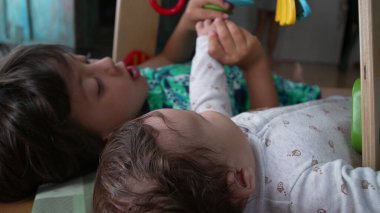 Genç bir çocuk bebek elini tutarak yerde yatıyordu, gözleri kapalıydı, çocukluk yıllarında kardeşlerin bağ kurduğu hassas ve huzurlu bir anı gösteriyordu.