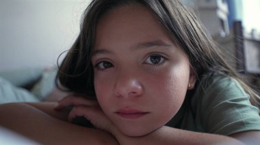 Başı elleri üzerinde uzanmış, dik dik bakan genç bir kız. Sakin ifadesi sakin ve huzurlu bir atmosfer yaratıyor, sessiz bir yansıma hissi veriyor.