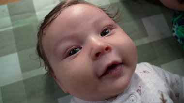 Bir bebeğin yere uzanmış, gözleri açık sevinçle gülümseyen, saf mutluluğu ve bebek merakını yakalayan bir görüntüsü.