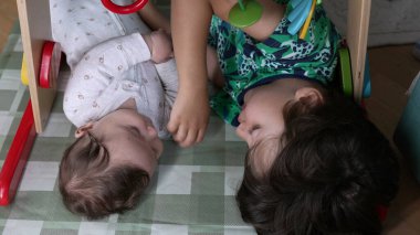 Küçük çocuk kardeşinin yanında dinleniyor. İkisi de ahşap bir spor salonunun altında birbirlerine sessizce bakıyor. Bir hasırdaki kardeşler arasında sakin ve samimi bir an