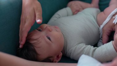 Bebek kanepede yatarken bir el nazikçe başını okşuyor. Sakin, şefkatli bir an bebek ve bakıcı arasındaki yakınlığı ve şefkati yansıtıyor.