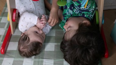 Küçük çocuk kardeşinin yanında dinleniyor. İkisi de ahşap bir spor salonunun altında birbirlerine sessizce bakıyor. Bir hasırdaki kardeşler arasında sakin ve samimi bir an