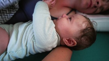 Uyuyan annenin yanında uzanan bebek, tetikte bir ifadeyle etrafa bakıyor, sabahın erken saatlerinde sakin bir bağ kurma anı yaratıyor.