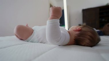 Bebek bacaklarıyla yatakta uzanıyor, usulca çevreye bakıyor. Sakin bir atmosfer çocukluğun masumiyetini ve merakını yakalar rahat ve besleyici bir ev ortamında