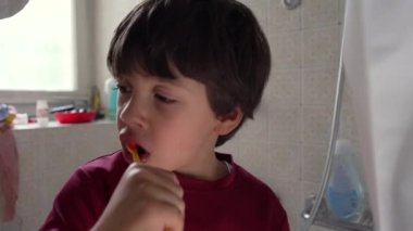 Oğlan diş fırçalama, yakın görüş, odaklanmış ifade, sabah hijyen rutini, günlük basit iş, diş bakımı anı, banyo ortamında diş fırçalama.