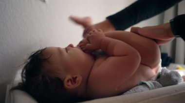 Bebek masasını değiştiriyor, anne kucağında bebek bezi, çocuk hafifçe gülümsüyor, rutin bakım, her gün ebeveyn ile etkileşim, rahatlık ve bakım, yakın ilişki.