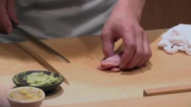 Suşi şefi taze balık fileto dilimliyor, ellerin yakın çekimi ahşap tezgahta sashimi kesiyor, keskin ve hassas bıçak becerileri, geleneksel Japon mutfağı hazırlığı, yakınlarda wasabi var.
