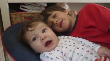 Bebek bir fedaiye uzanıyor, ağabeyinin yüzüne dokunuyor, evde sakin bir aile ortamında nazik bir kardeş etkileşimi.