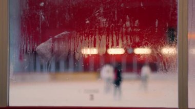Buz pateni pisti manzaralı sisli camlar, arka planda bulanık figürler, penceredeki buğulanma, kış sporları sahnesi, hokey sahası atmosferi, soğuk hava detayları.