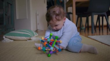 Bebek yerde uzanıyor, renkli bir oyuncağa uzanıyor, dokunsal oyunlara takılıyor, motor becerilerini geliştiriyor, oyuncağı ev ortamında merakla keşfediyor.