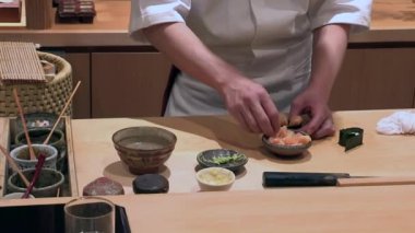 Suşi şefi suşi rulolarını birleştiriyor, geleneksel Japon mutfağı hazırlıyor, tezgahta çeşitli kase ve malzemeler var, odaklanmış ve yetenekli eller iş başında.