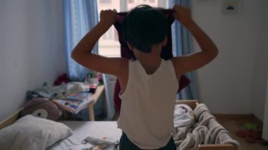 Genç çocuk, evde sakin bir sabah rutini sırasında yatak odasında gömlek giyip güne hazırlanıyor.