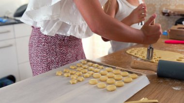 Yanında bir oğlan parçaları şekillendirirken genç bir kızın mutfak aletiyle hamur sıkıştırdığı fotoğraf. Olay yeri, evde pişirme sürecini eğlenceli ve yaratıcı bir şekilde yakalıyor.