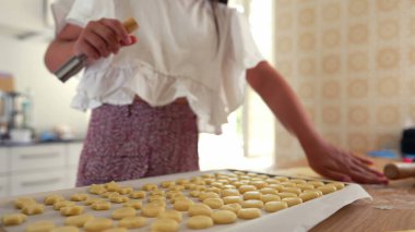 Küçük hamur parçalarını fırın tepsisine dizen genç bir kızın yakın plan çekimi. Arka planda daha çok hamuru şekillendiren bir oğlan var. Elle pişirme süreci