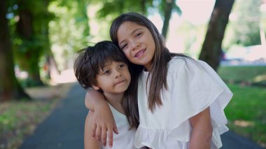 Genç bir kız, koluyla bir oğlanı sarıyor. Parktaki patikada dikilirken başını ona doğru eğiyor. Gerçek bir kardeş dostluğu ve şefkat anı.