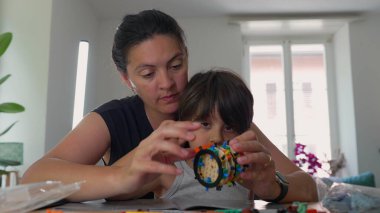 Anne ve genç çocuk bir yapı etkinliği sırasında parçaları dikkatlice istifliyor, birlikte çalışırken dikkatle odaklanıyorlar, ev ortamında ekip çalışması ve konsantrasyonu vurguluyorlar.