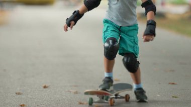 Genç çocuk kaykayını yerleştiriyor ve patikada sürmeye başlıyor. Kask ve koruyucu giysiler giyerek duruşunu düzeltir ve denge ve hareketlerine odaklanarak aktif olarak geri çekilir.