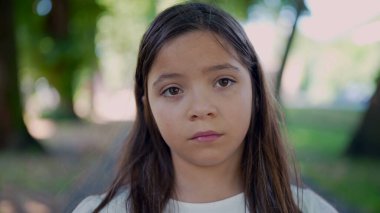 Arka planda yeşilliklerle çevrili, ciddi ve düşünceli bir ifadeyle dışarıda duran bir kız. Bakışları derin düşüncelere ya da duygusal bir ana işaret ediyor.