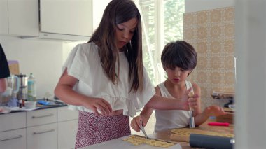 Genç bir kız mutfak aletleriyle hamur sıkıştırmaya odaklanırken bir oğlan onun yanında dikkatlice çalışıyor. bir ev yapımı oturum sırasında konsantrasyon ve beceri