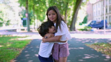 Genç bir kız parkta duruyor, kollarını beline dolayan bir çocuğa sarılıyor. Sıcak ve sevecen bir kardeş anı. Huzurlu, yeşil bir geçmişi var.