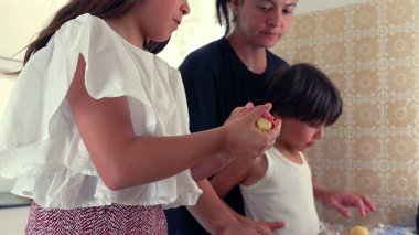 Anne ve oğlan arka planda izlerken, genç kız elleriyle hamuru şekillendiriyor. Bir dakikalık aile birlikteliği ve mutfakta öğrenme.