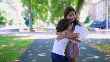 Genç bir kız parkta duruyor, kollarını beline dolayan bir çocuğa sarılıyor. Sıcak ve sevecen bir kardeş anı. Huzurlu, yeşil bir geçmişi var.