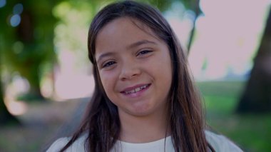 Arka planda yeşilliklerle çevrili neşeli bir ifadeyle dışarıda gülümseyen bir kız. Samimi gülüşü mutluluk ve pozitiflik hissi veriyor.